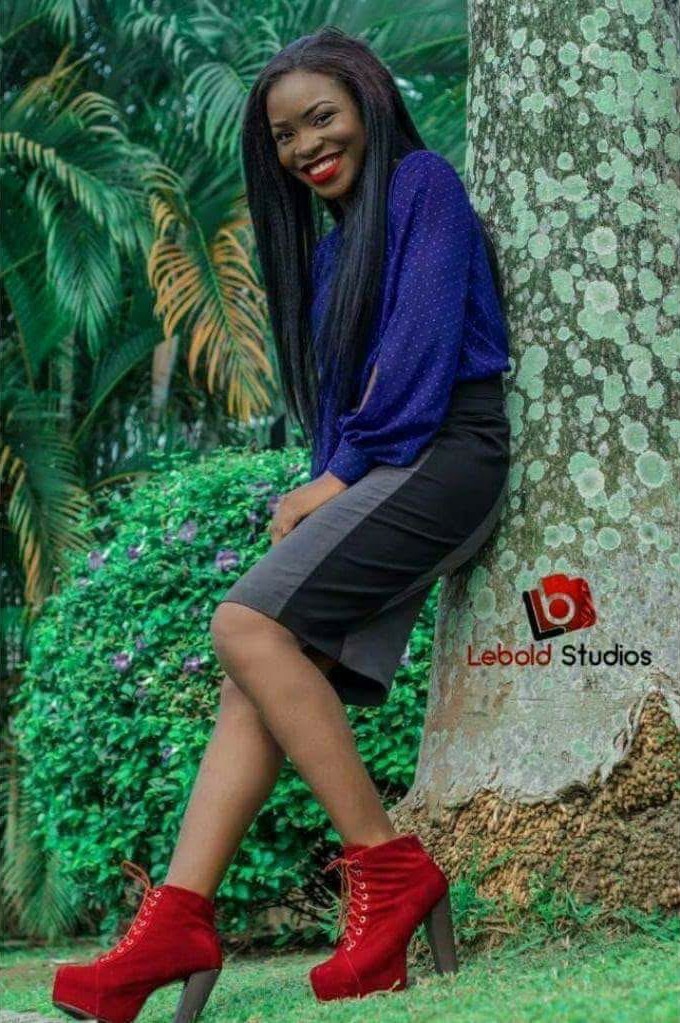 MaryAlice smiling against a tree in a blue blouse, grey skirt and red suede heeled boots