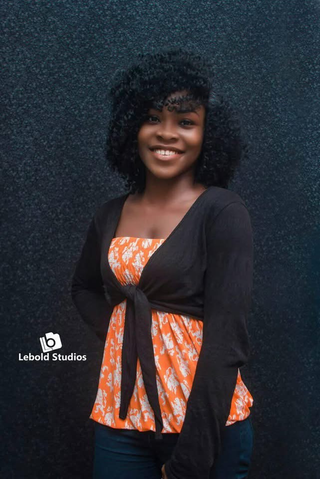 MaryAlice with curly hair, smiling in an orange top and black wrap cardigan